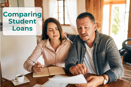 A woman and man sit at a table comparing loan options. She holds a pen over a spiral notebook and he holds a piece of paper they are looking at together.